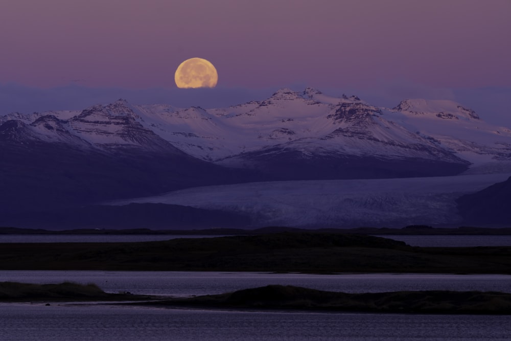 the moon is setting over a mountain range