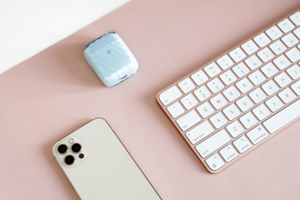 um teclado, telefone e mouse em uma superfície rosa