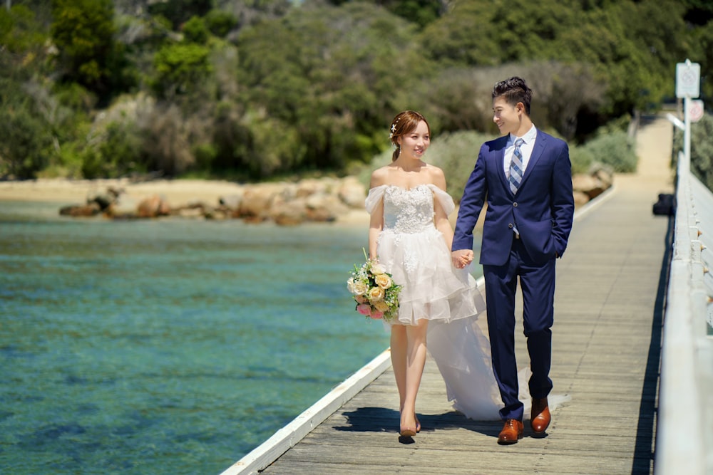 a bride and groom walking along a pier