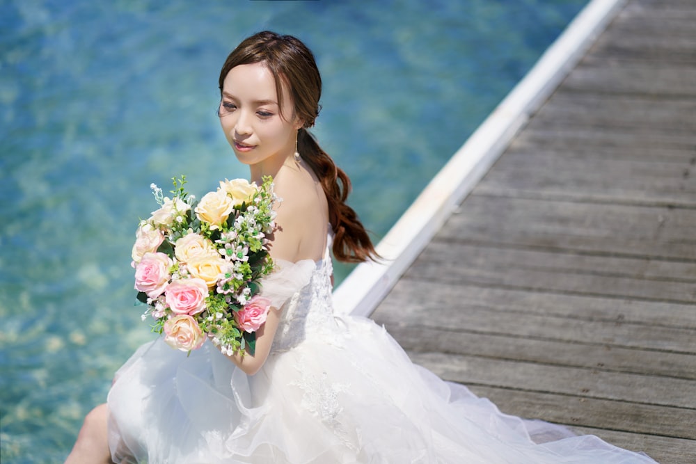 a woman sitting on a dock holding a bouquet of flowers