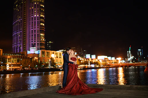 A chic couple dressed in elegant evening wear walking hand-in-hand under soft city lights.