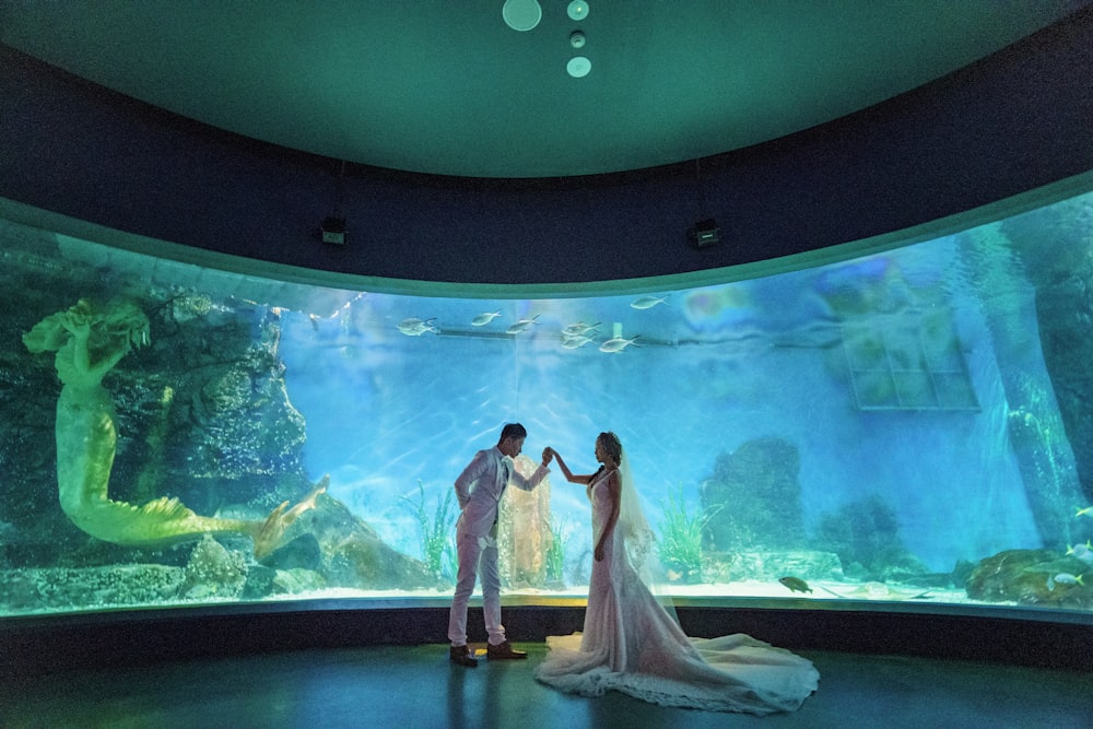 a bride and groom standing in front of a large aquarium