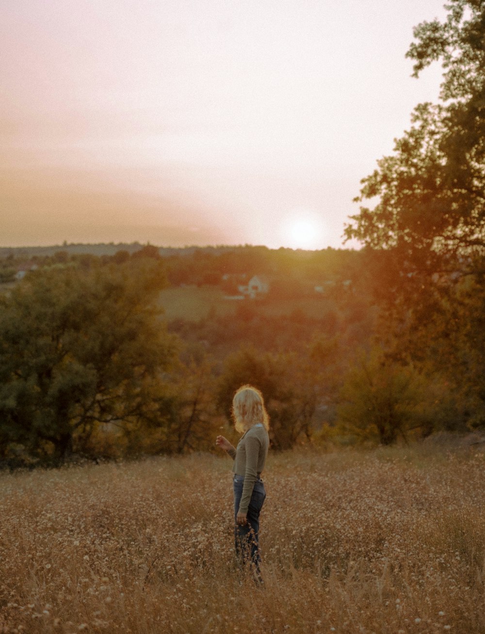 a woman standing in a field with trees in the background