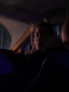 A blurry image capturing a person inside a vehicle, with dim lighting creating a mysterious atmosphere. The features of the person are indistinct due to motion blur.