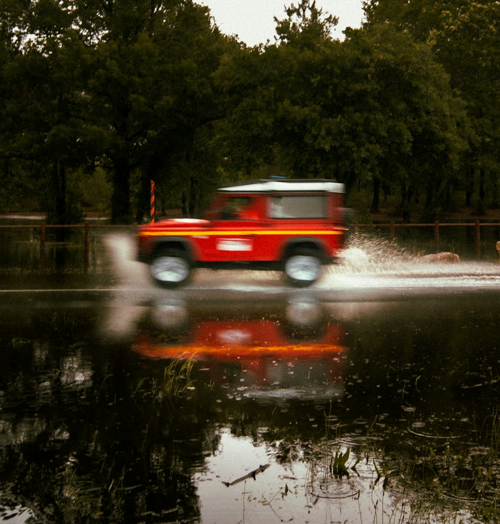 a red truck driving down a street next to a forest