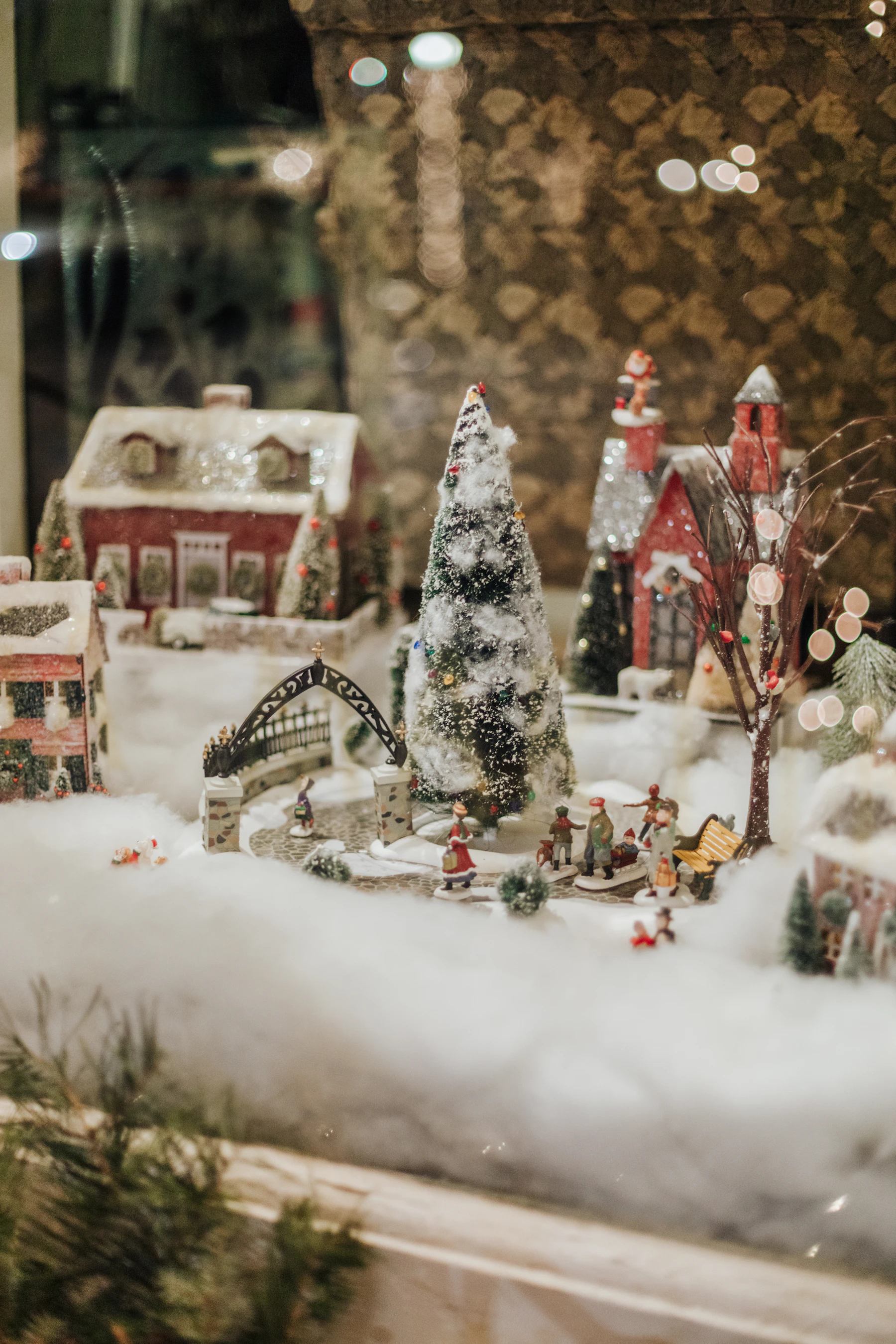 A shop-window village on cotton snow: glittered houses, a bottle brush tree and tiny skaters crossing a bridge