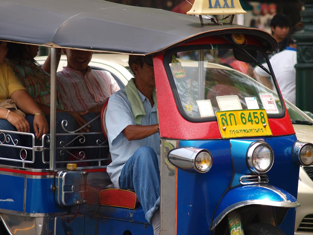 a man driving a blue and red tuk tuk