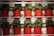 Rows of vibrant green plants are placed in bright red pots arranged neatly on white shelves. The pots have a subtle heart design embossed on the front, and the plants appear lush and healthy.
