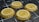 Four golden coins with different cryptocurrency logos are positioned in a grid-like arrangement on a dark, futuristic surface with intersecting white lines.