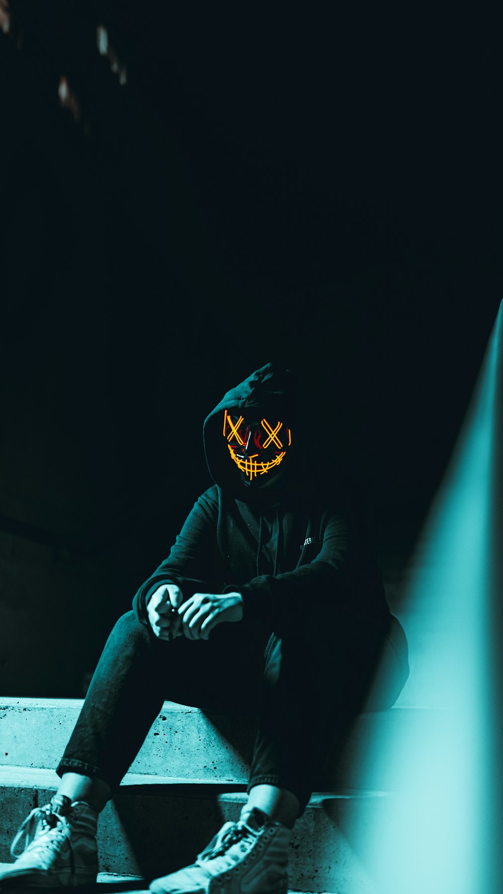 a person sitting on a step with a neon mask on