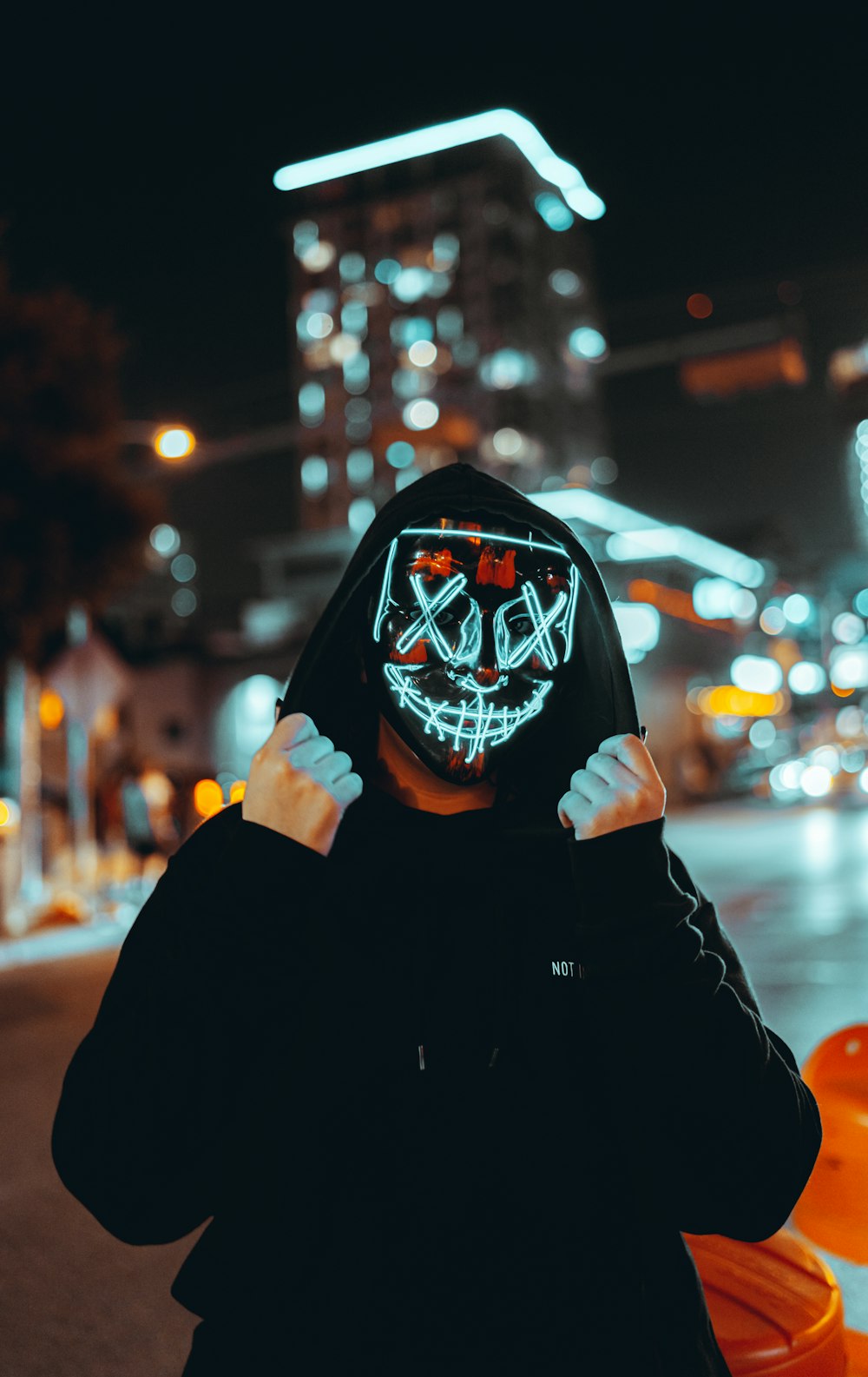 a person in a black hoodie wearing a neon mask