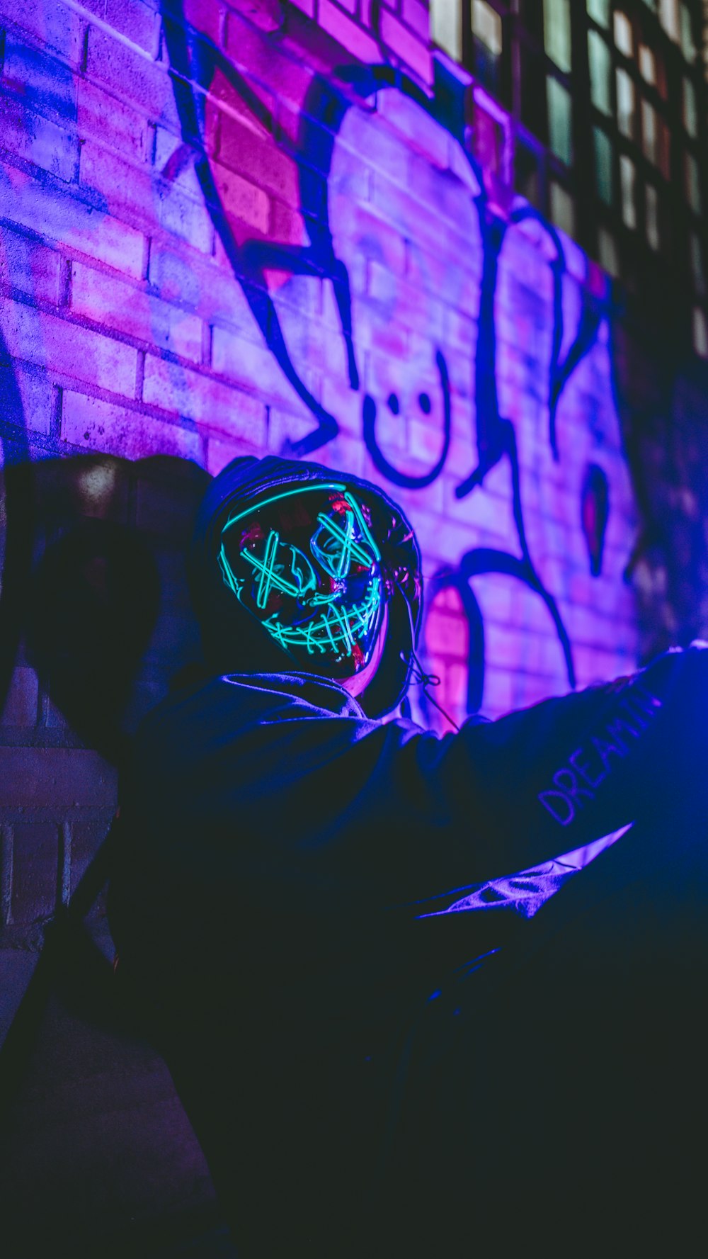 a man sitting in front of a brick wall with a neon sign on it