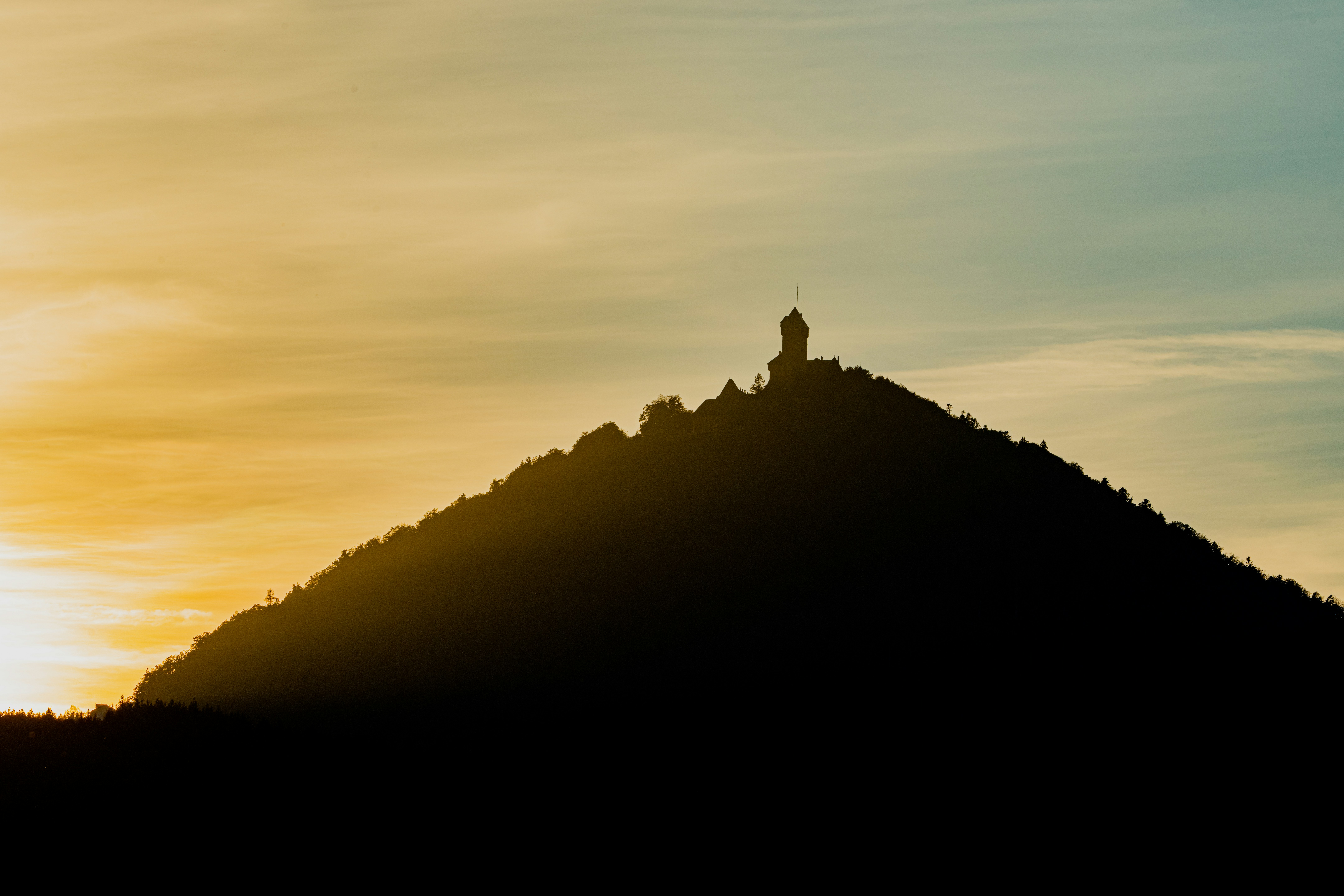 A silhueta de uma pessoa em pé no pico de uma montanha ao nascer do sol, representando liderança e visão.