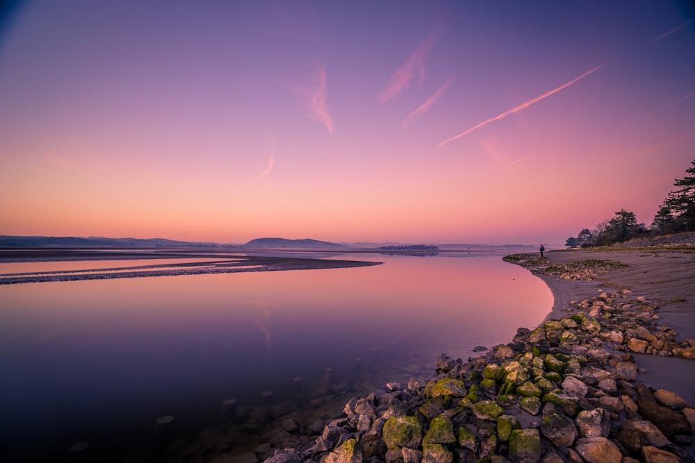 a person standing on the shore of a lake at sunset