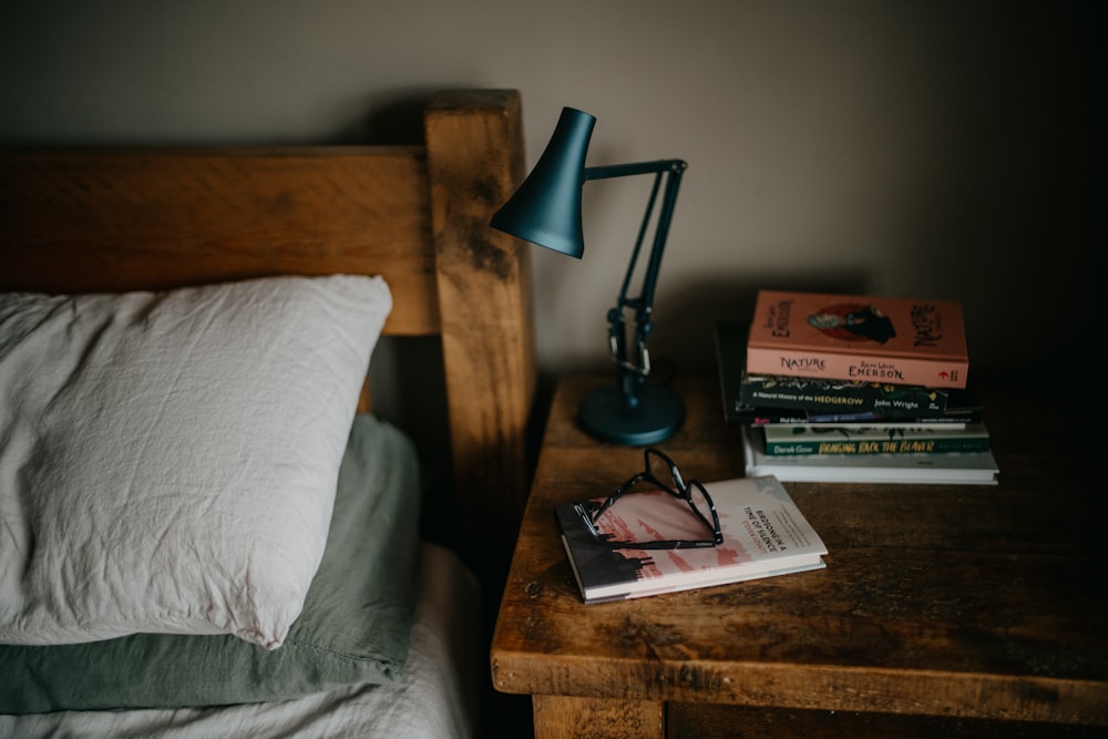 Una pila de libros sentados encima de una cama junto a una lámpara