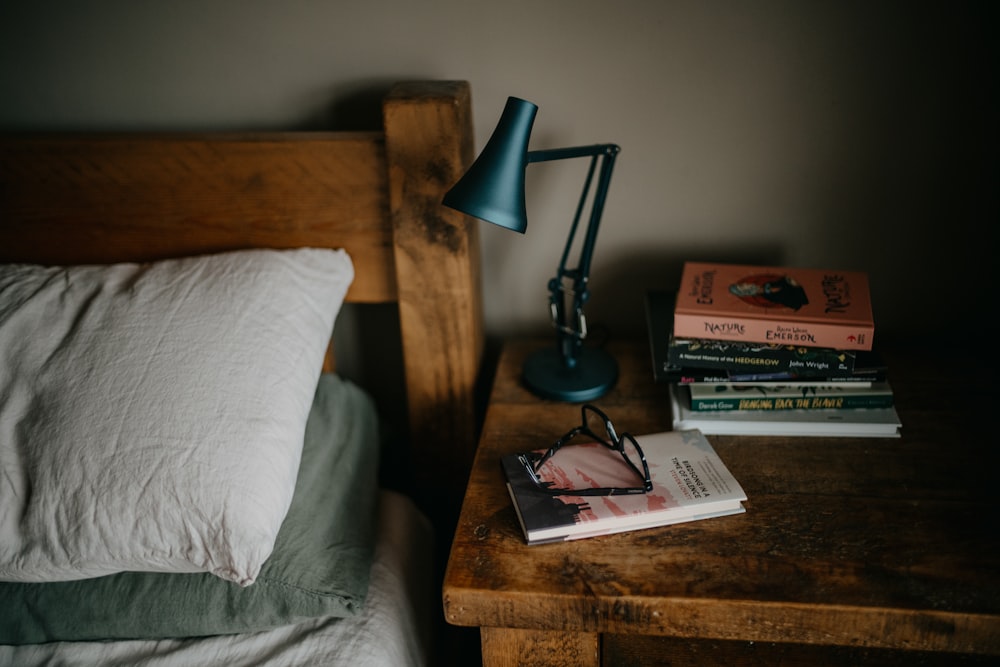 a stack of books sitting on top of a bed next to a lamp