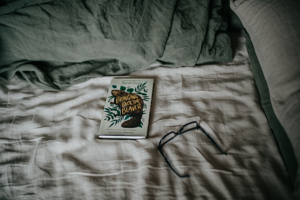 a book sitting on top of a bed next to a pair of glasses