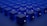 A series of identical blue cubes are arranged in a grid pattern on a flat surface. Each cube is illuminated with a subtle light, casting soft shadows. A symbol resembling the Tezos blockchain logo is visible on the sides of the cubes.