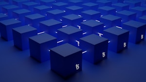 A series of identical blue cubes are arranged in a grid pattern on a flat surface. Each cube is illuminated with a subtle light, casting soft shadows. A symbol resembling the Tezos blockchain logo is visible on the sides of the cubes.