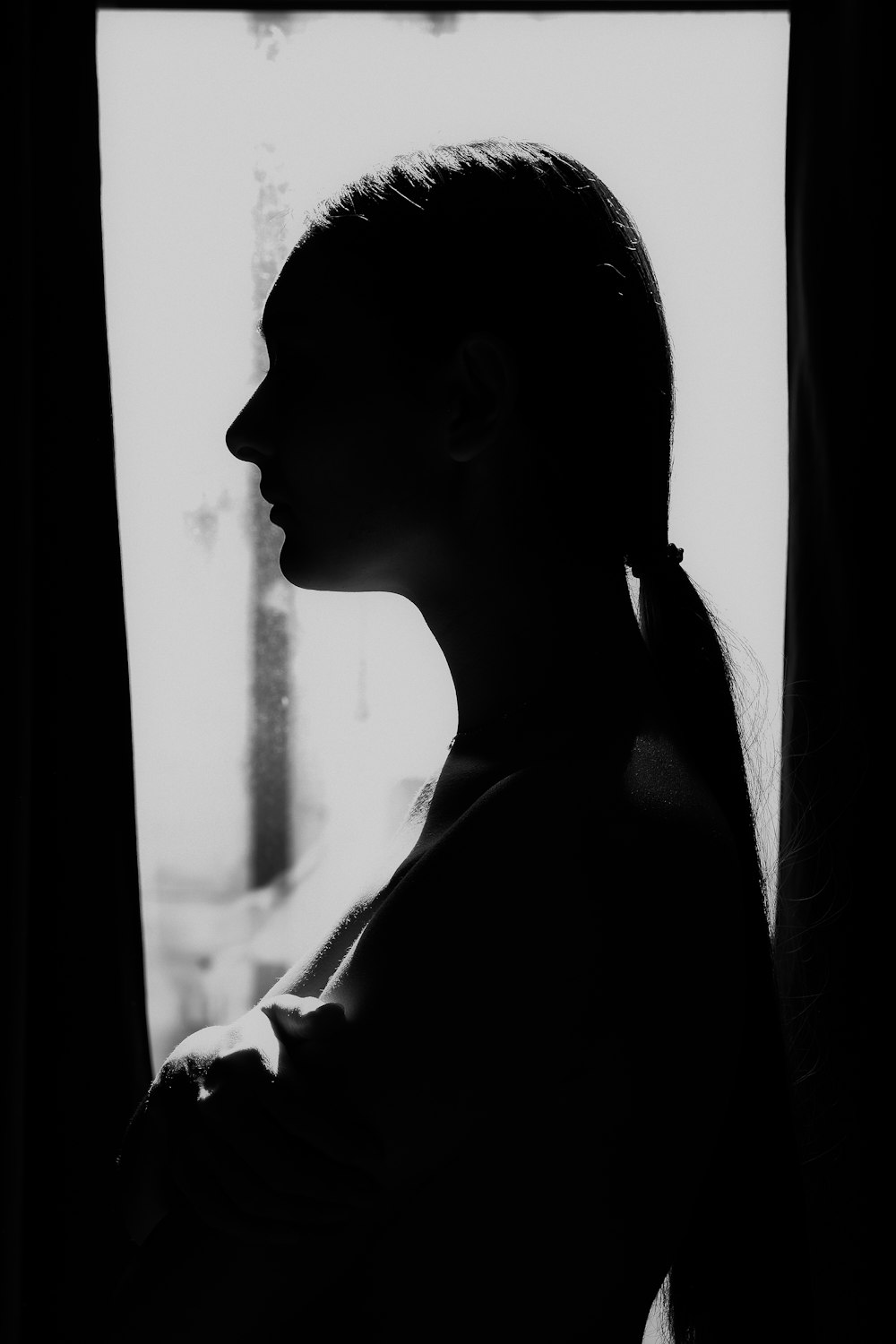 a black and white photo of a woman looking out a window