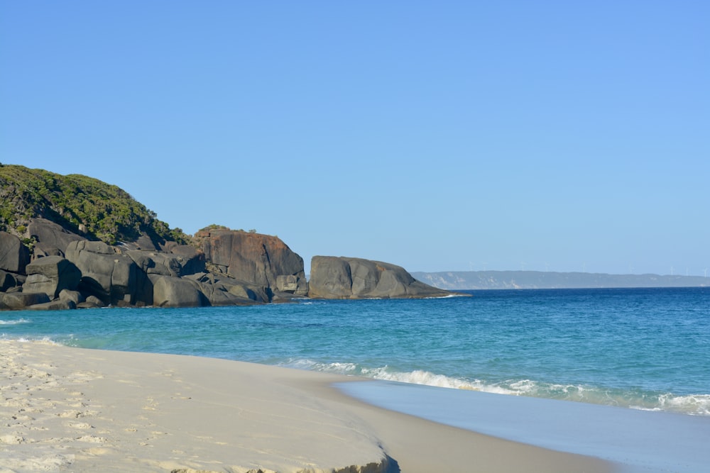 a sandy beach next to the ocean with rocks in the background