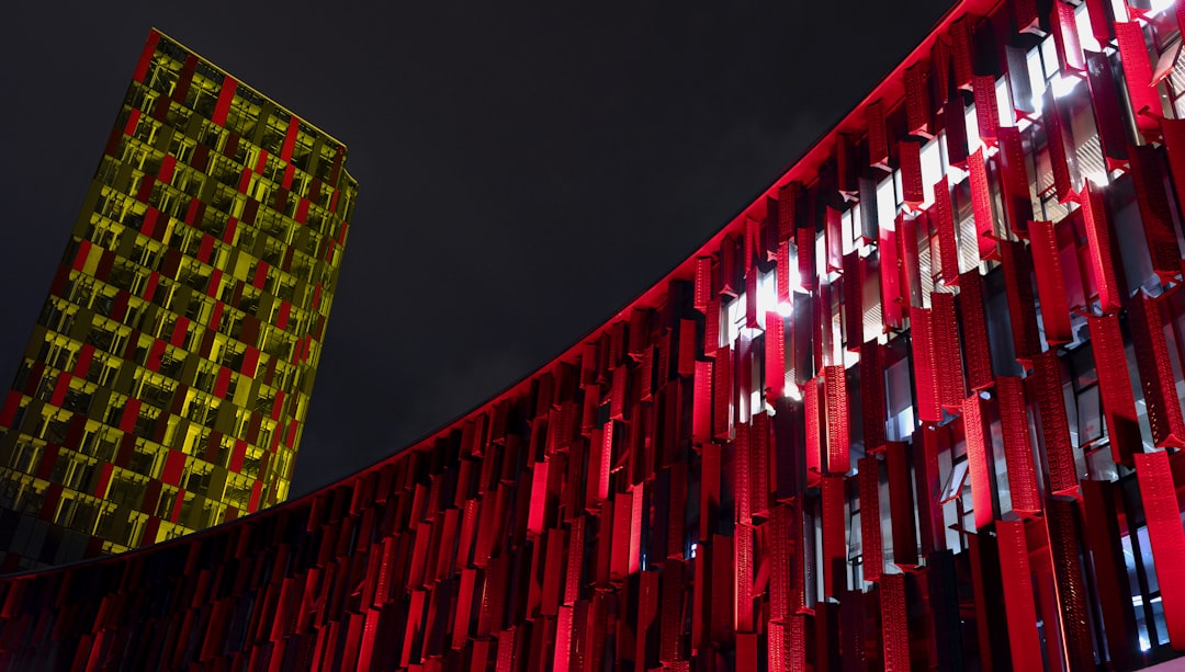 a tall red building next to a tall yellow building, Air Albania stadium at night