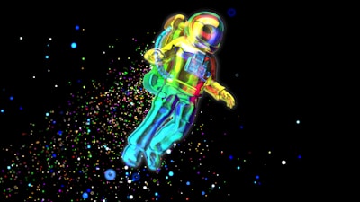 A colorful astronaut floats in the vastness of space, surrounded by a myriad of bright, multicolored particles. The suit reflects vibrant hues of yellow, green, blue, and red, creating a captivating visual. The background is a deep black, enhancing the vivid display of colors.
