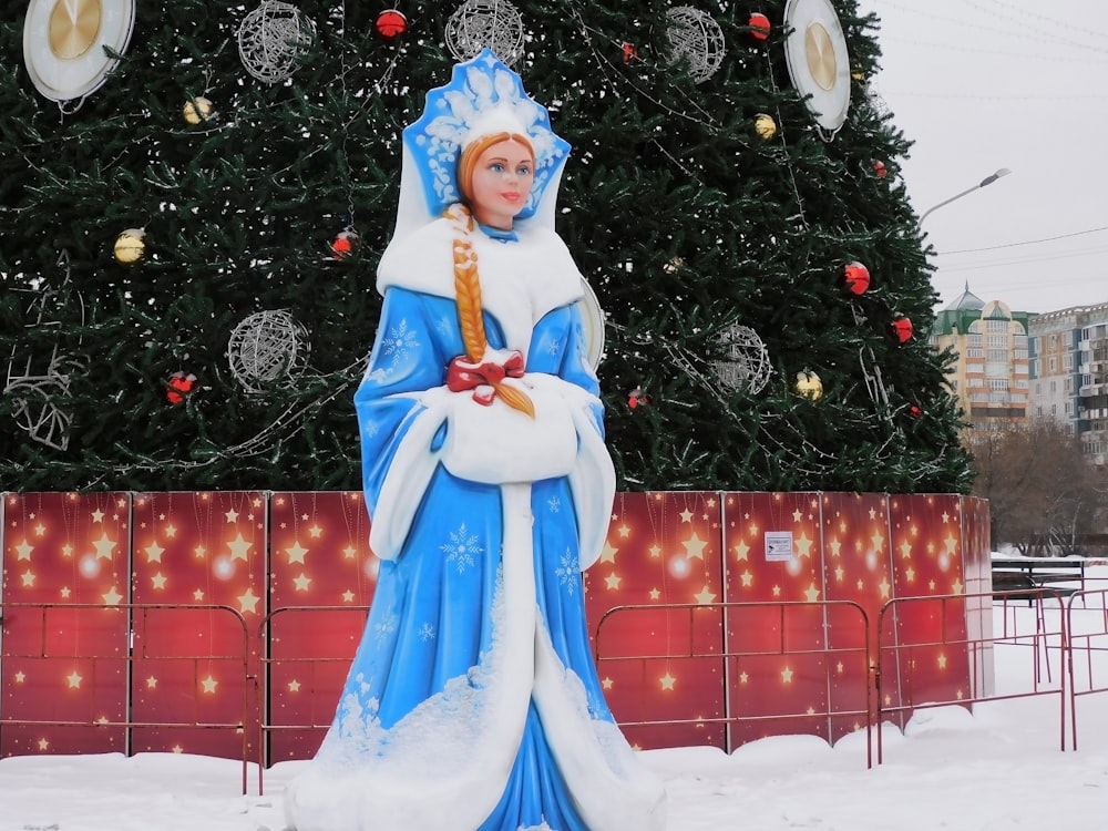 a statue of a woman standing in front of a christmas tree