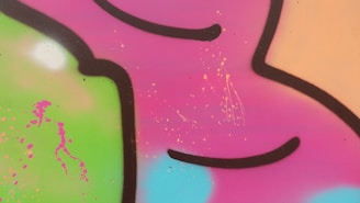 Bright and vibrant graffiti art with abstract shapes. Bold black outlines contrast against a colorful background featuring shades of pink, green, orange, and blue. Splattered paint adds texture to the artwork.