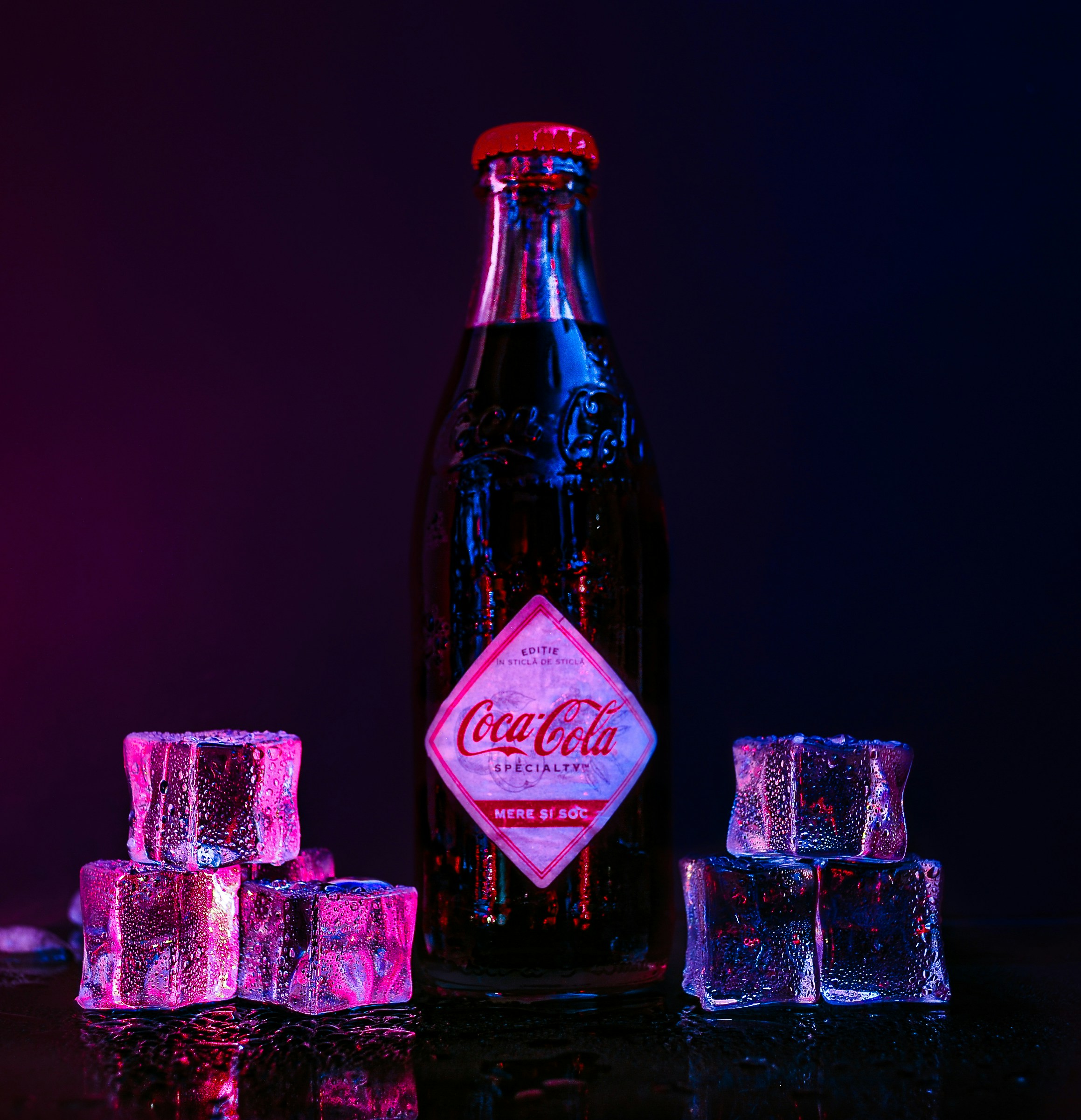 Una bottiglia di Coca Cola seduta accanto a cubetti di ghiaccio