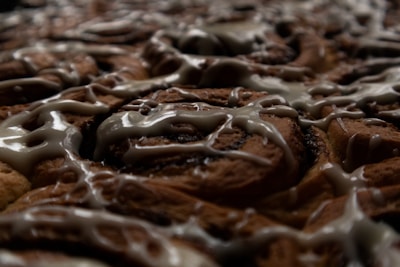 A close-up view of freshly baked pastries drizzled with icing. The image highlights the swirls of the brown pastry dough and the glossy texture of the light-colored icing.