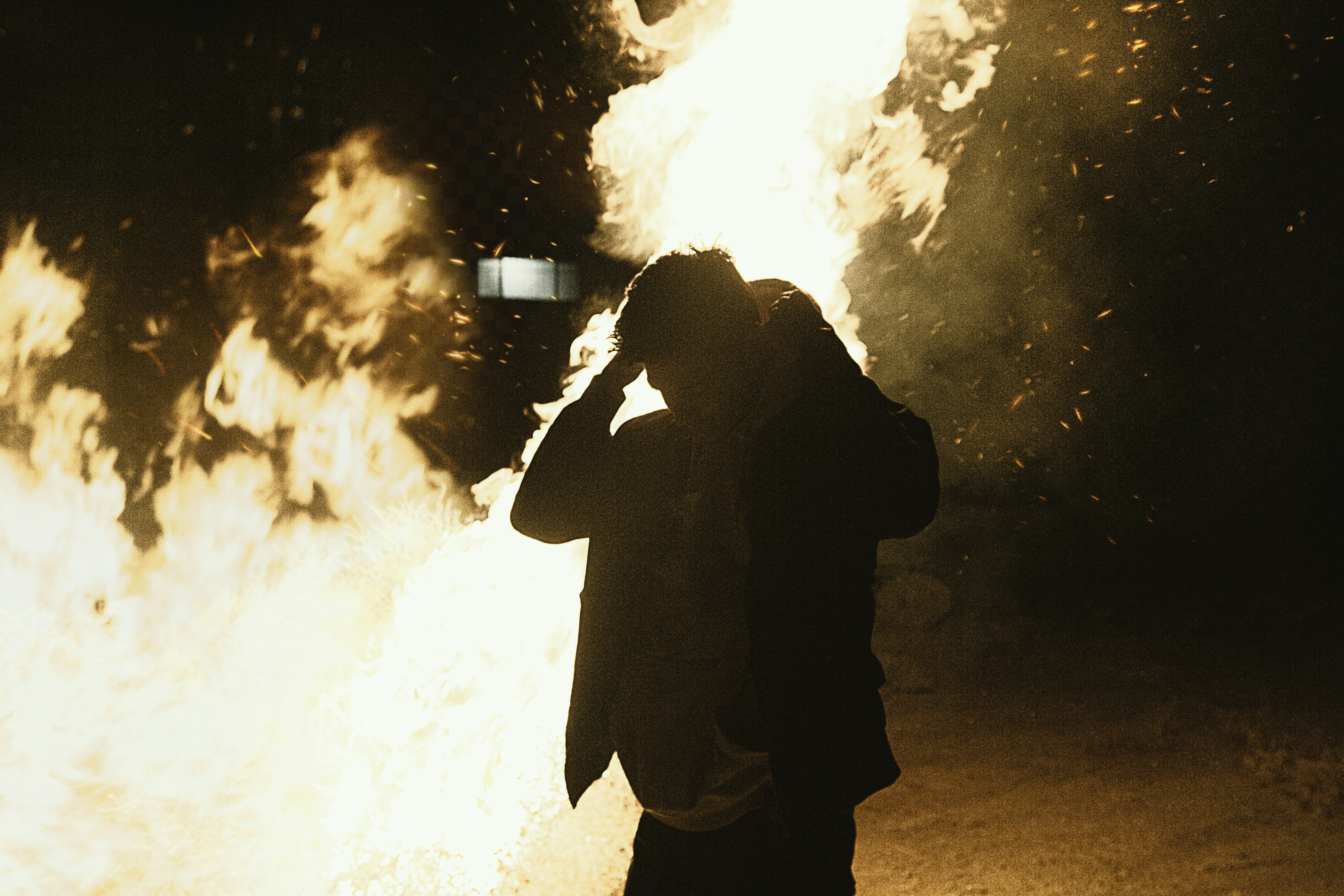 a man standing in front of a fire with a cell phone to his ear