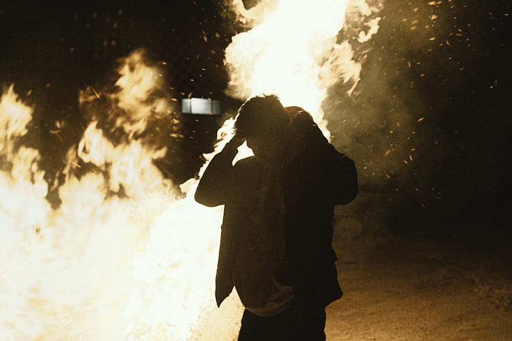 a man standing in front of a fire with a cell phone to his ear