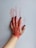 A hand with black-painted nails is pressed against a surface, leaving a smeared red paint imprint. The fingers and palm are covered with red paint, and the background is a plain, light-colored surface.