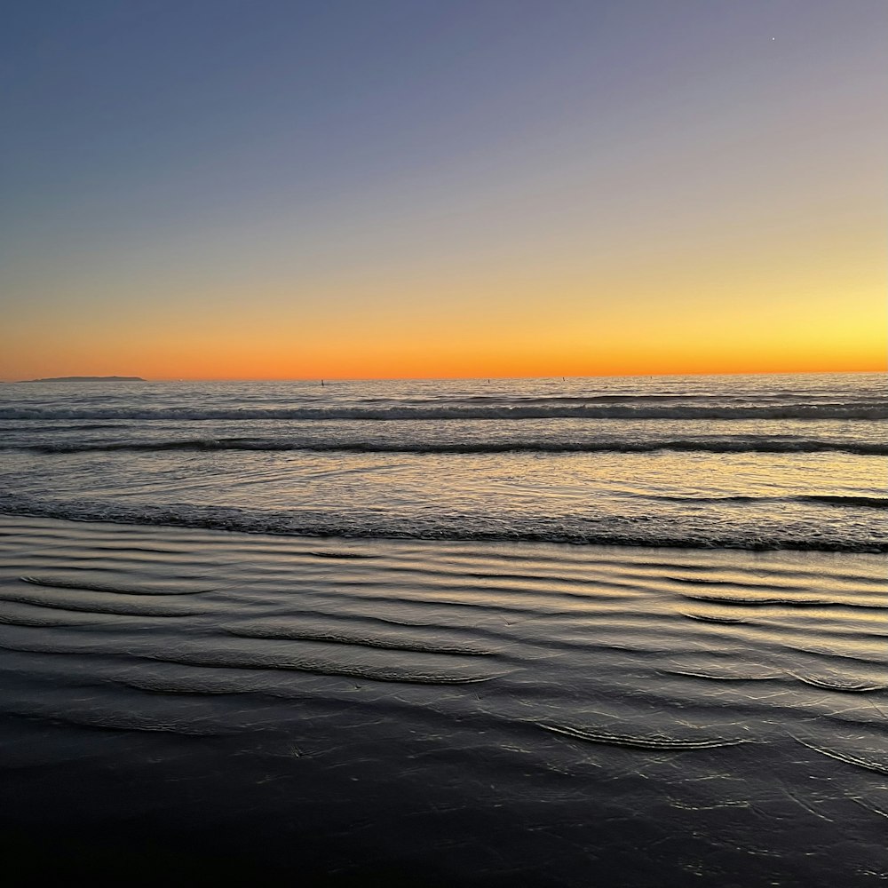 the sun is setting over the water at the beach