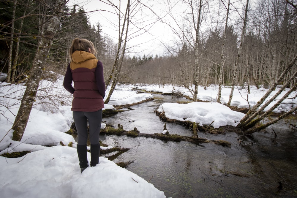 a woman standing in the snow near a stream