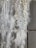 A close-up view of a textured wall with efflorescence. The surface appears rough and uneven, with white salt deposits covering sections of the gray concrete tiles.
