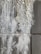 A close-up view of a textured wall with efflorescence. The surface appears rough and uneven, with white salt deposits covering sections of the gray concrete tiles.