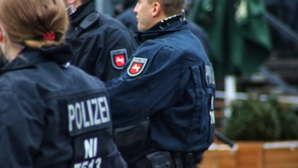 Several individuals in dark blue uniforms featuring patches with the word 'POLIZEI' on the back. The patches and uniform details suggest they are likely police officers, standing in an outdoor environment possibly during an event or patrol.