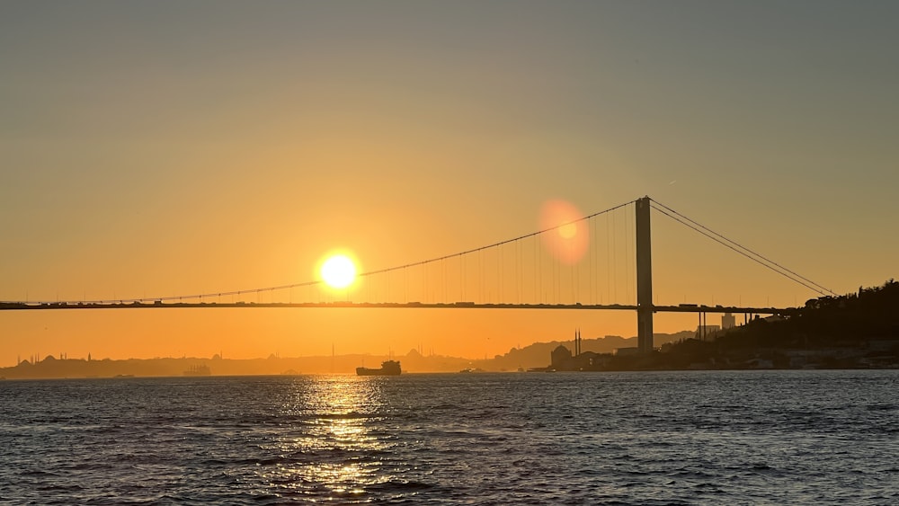 the sun is setting over a bridge over a body of water