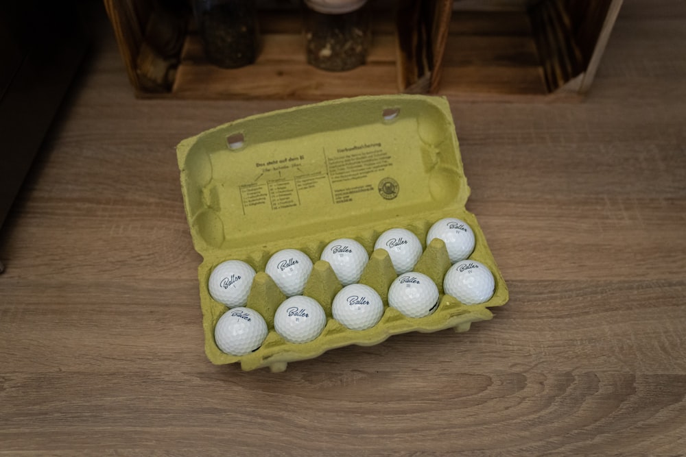 a dozen golf balls in a carton on a wooden floor