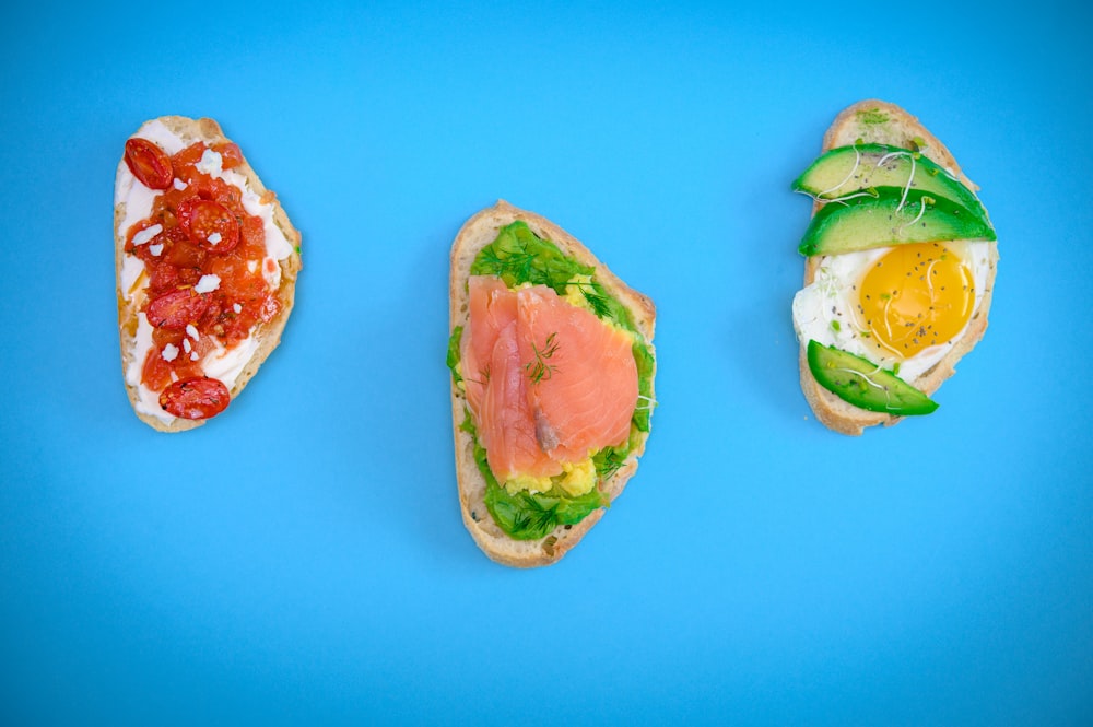 three sandwiches are arranged on a blue surface