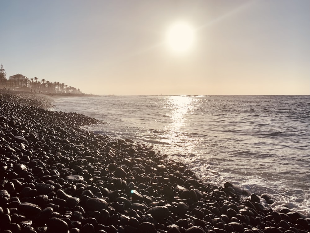 the sun shines brightly over the ocean on a rocky beach