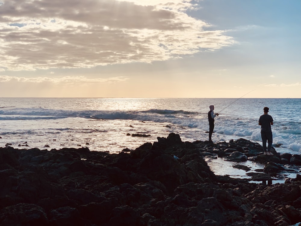 a couple of people standing on top of a rocky beach