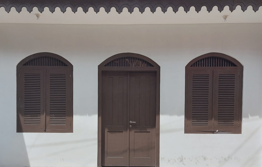 a white building with three brown doors and three windows