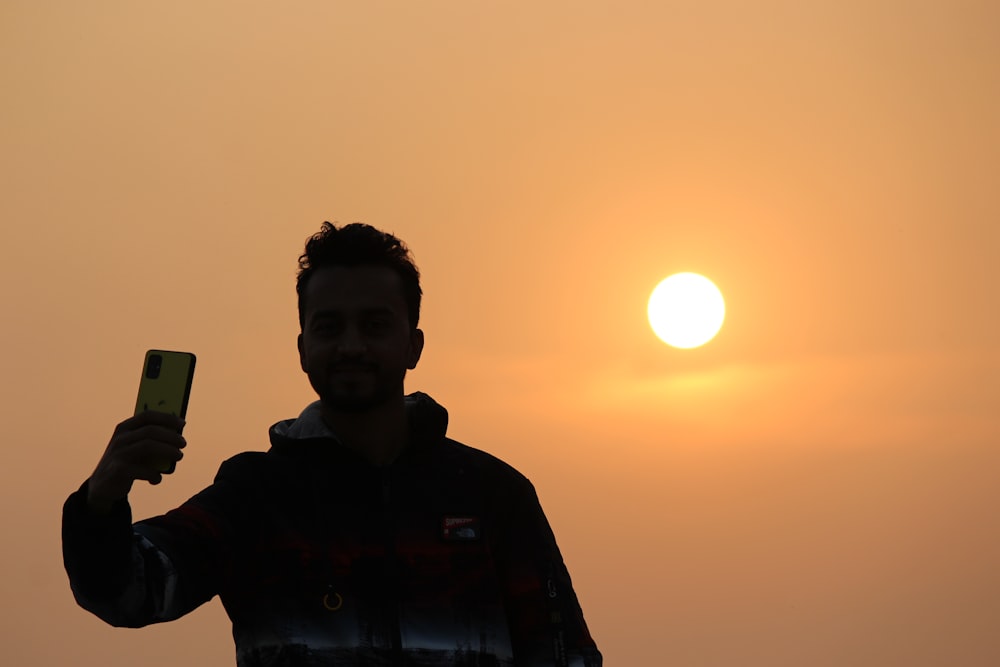 a man holding up a cell phone in front of the sun