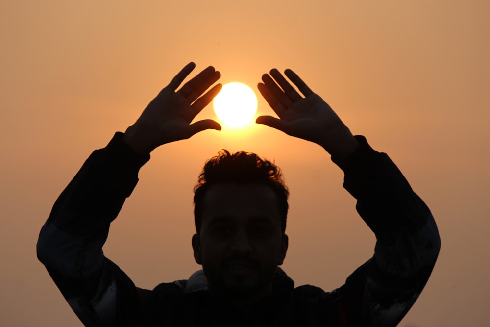 a man holding his hands up to the sun