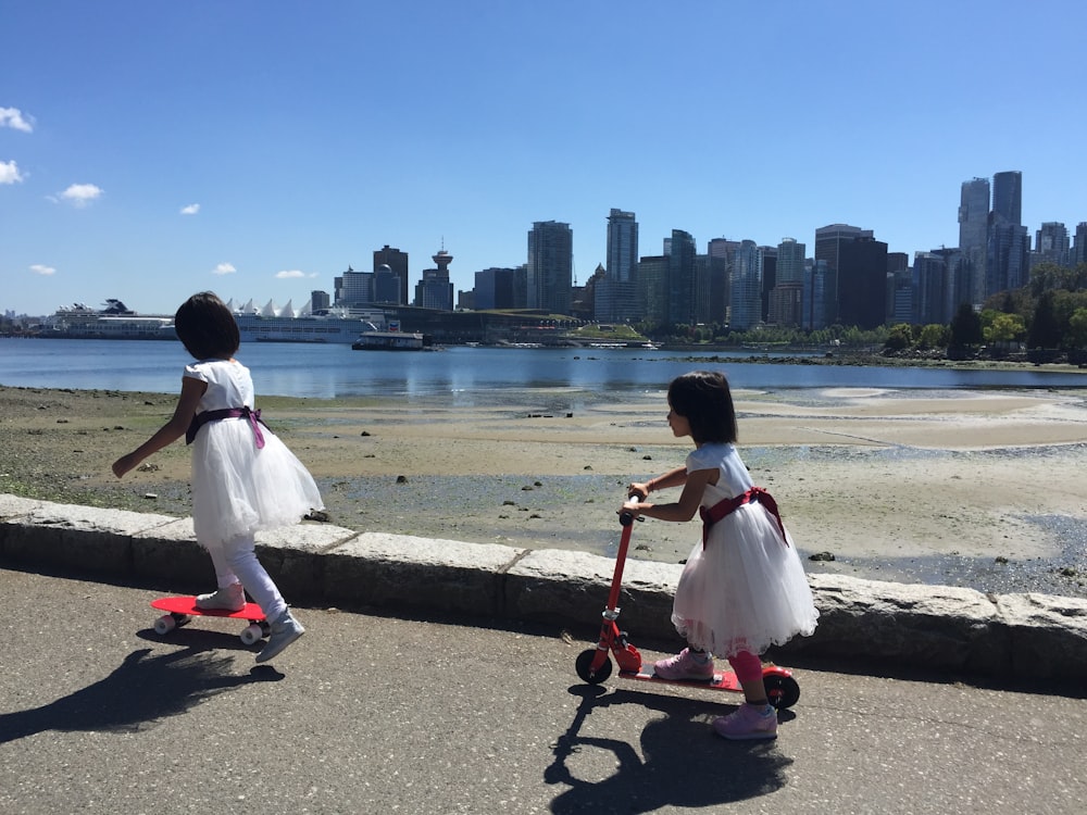 Due bambine vestite stanno guidando scooter vicino all'acqua