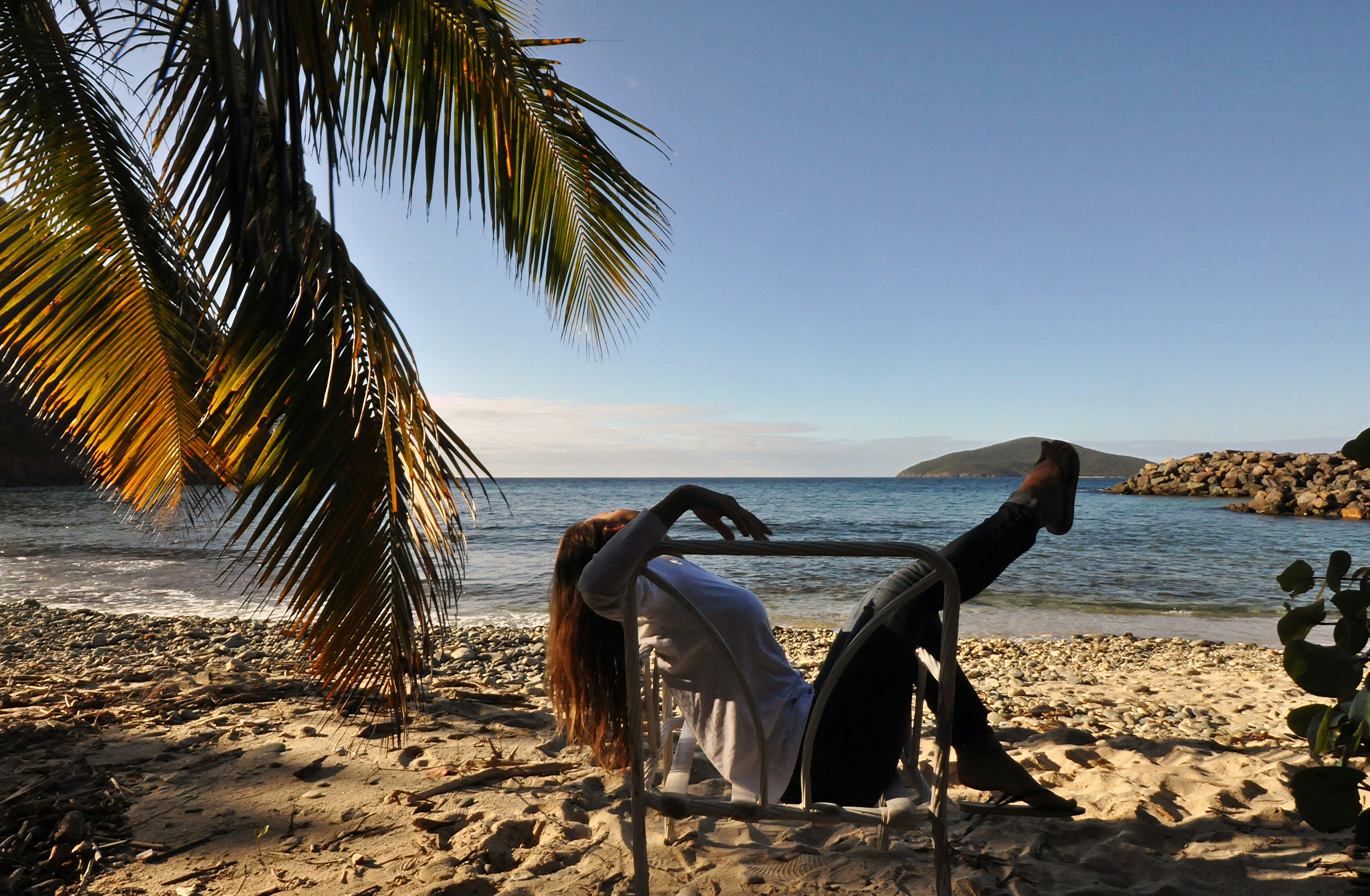 A woman reclines on a beach chair in the late afternoon shade with Atlantic Ocean and Han Lollick island on the horizon.