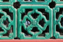 A series of decorative green ceramic tiles with intricate floral patterns and swirls, bordered with a red base. The tiles form a symmetrical design and have a glossy finish.